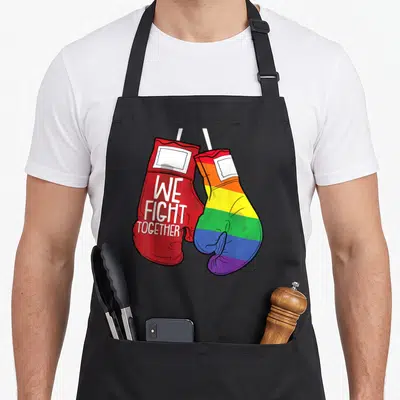 Tablier de cuisine noir avec deux gants de boxe croisés, un rouge et un aux couleurs de l'arc-en-ciel portant l'inscription We Fight Together.