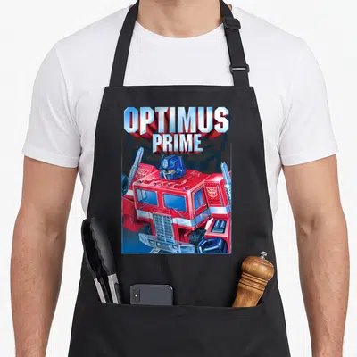 Tablier de cuisine noir avec une illustration colorée représentant Optimus Prime en version camion rouge et bleu sous son nom imprimé.
