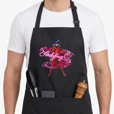 Tablier de cuisine noir avec Ladybug en tenue rouge et un petit compagnon rose entourés de magie.
