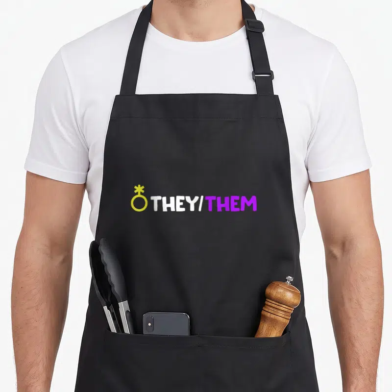 Tablier de cuisine noir avec le texte They/Them et un symbole non binaire jaune sur fond uni.