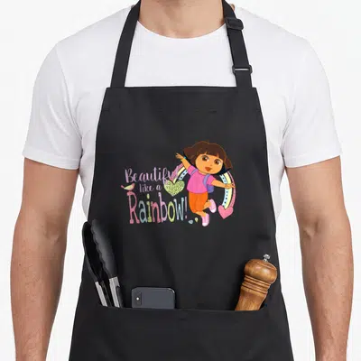 Tablier de cuisine noir avec Dora la exploratrice et l'inscription « Magnifique Comme un Arc-en-ciel » colorée.