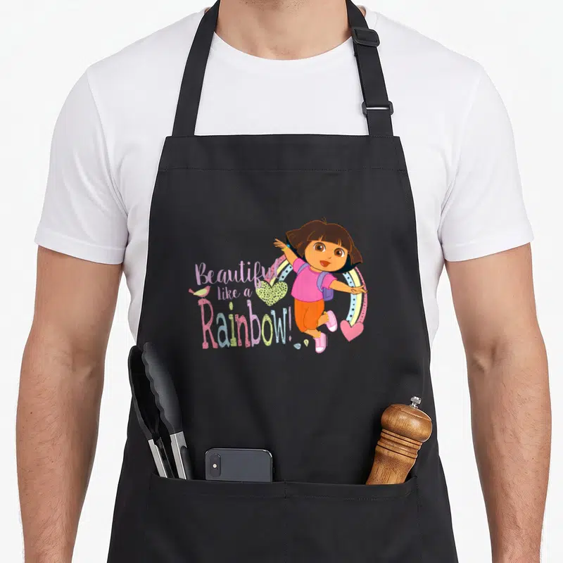 Tablier de cuisine noir avec Dora la exploratrice et l'inscription « Magnifique Comme un Arc-en-ciel » colorée.