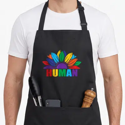 Tablier de cuisine noir avec une fleur multicolore et le mot HUMAN en lettres arc-en-ciel.