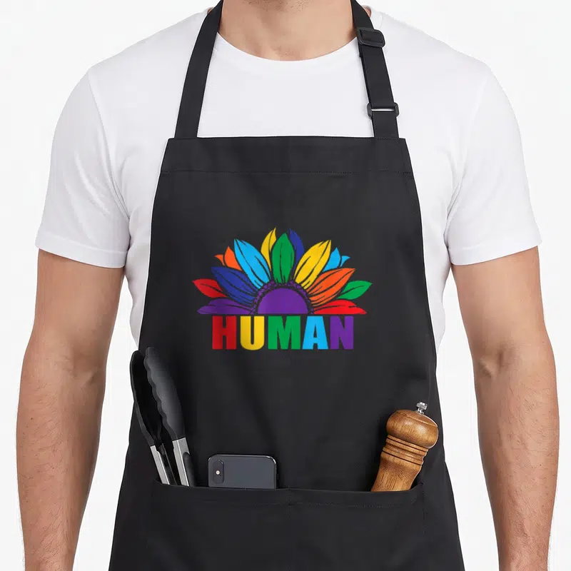 Tablier de cuisine noir avec une fleur multicolore et le mot HUMAN en lettres arc-en-ciel.