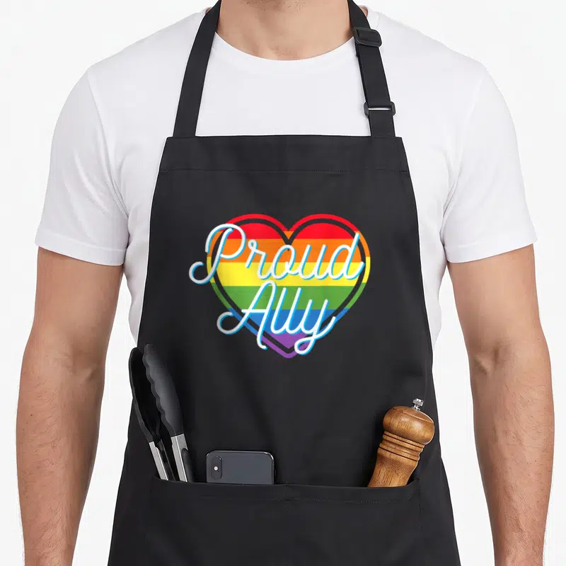 Tablier de cuisine noir avec un cœur arc-en-ciel et le texte Proud Ally en lettres blanches cursive.