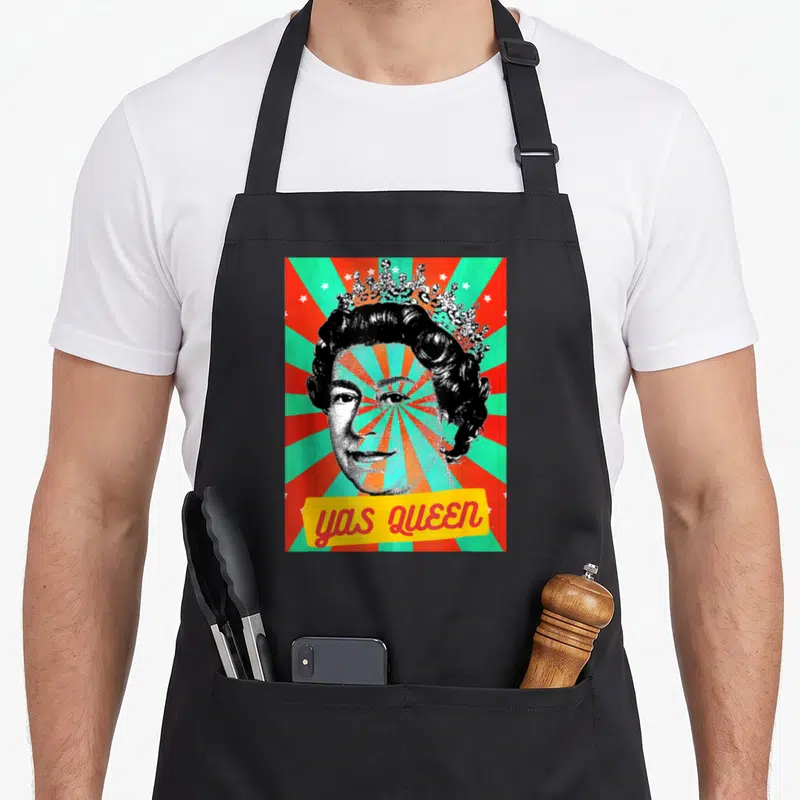 Tablier de cuisine noir avec illustration pop art d'une reine couronnée et texte Yas Queen sur fond rayé.