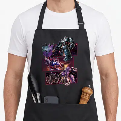 Tablier de cuisine noir avec illustrations Transformers Megatron Optimus Prime et logo Decepticon sur fonds spatiaux roses.