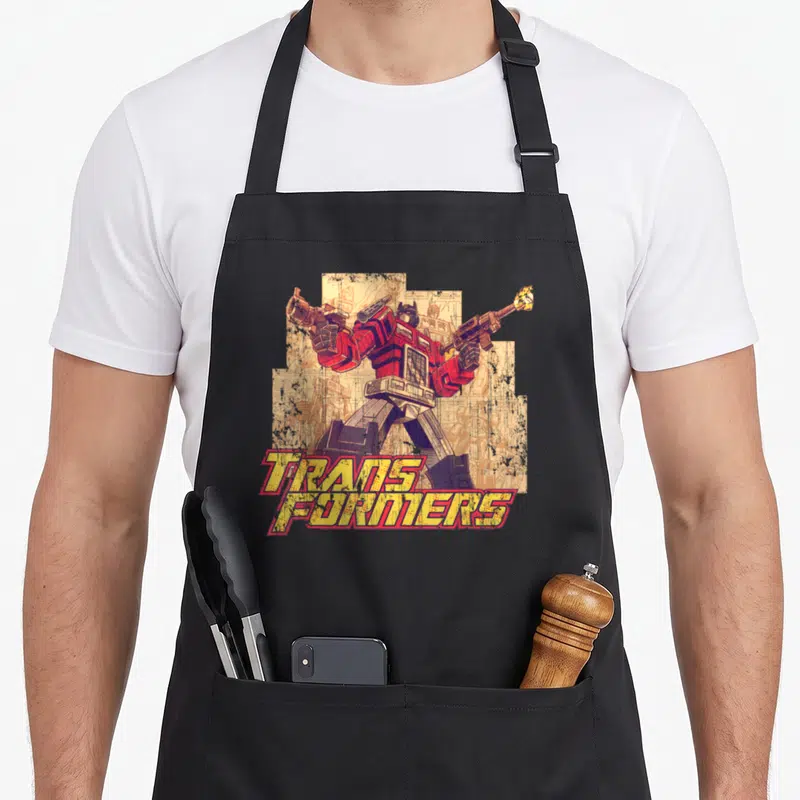 Tablier de cuisine noir avec illustration vintage d'Optimus Prime tenant deux armes et le logo TRANSFORMERS.