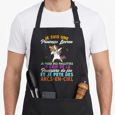 Tablier de cuisine noir avec une licorne blanche effectuant un dab et du texte coloré humoristique sur le devant.