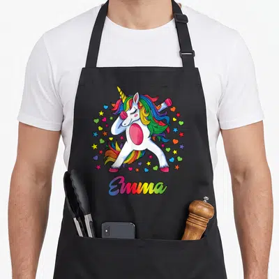 Tablier de cuisine noir avec une licone blanche aux cheveux multicolores effectuant un dab entouré d'étoiles et de cœurs colorés.