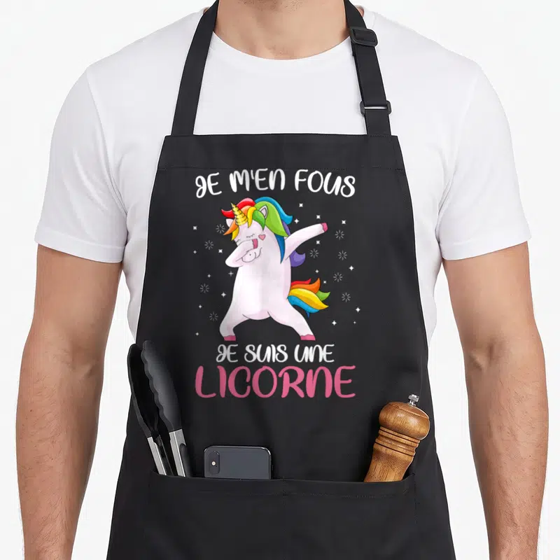 Tablier de cuisine noir avec une licorne rose effectuant un mouvement de danse dab entourée d'étoiles et du texte Je m'en fous je suis une licorne.