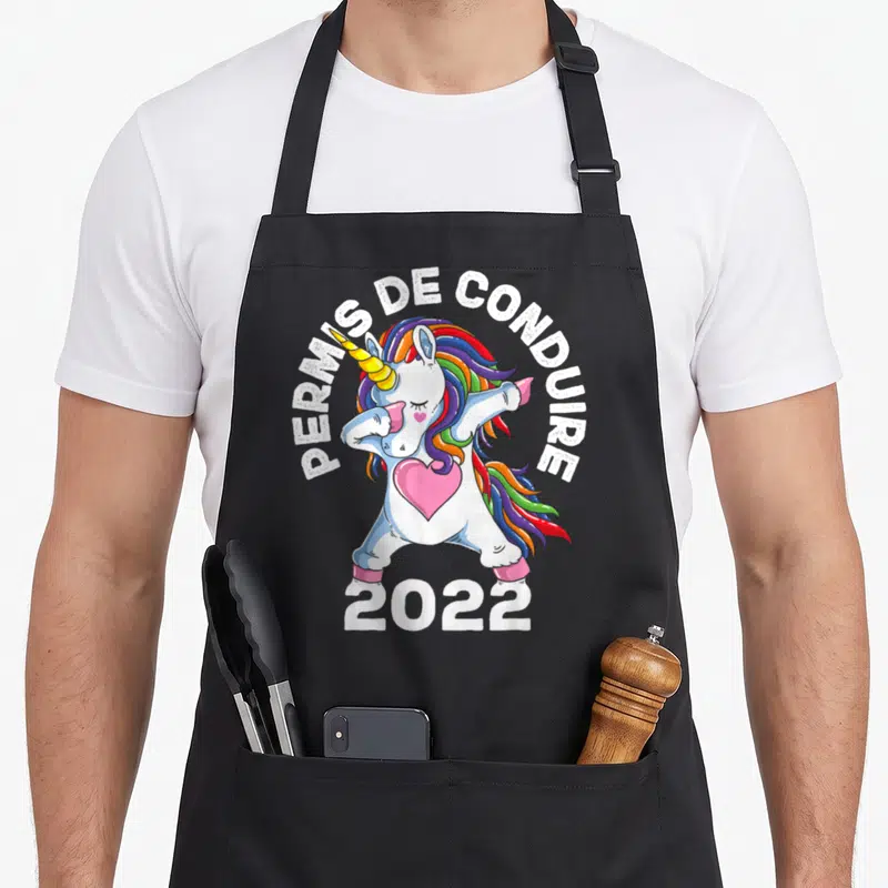 Tablier de cuisine noir avec une licorne blanche en train de faire un dab, entourée du texte Permis de conduire 2022 et d'un cœur rose.