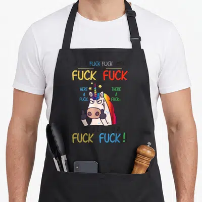 Tablier de cuisine noir avec licorne blanche aux deux doigts et texte multicolore provocant.