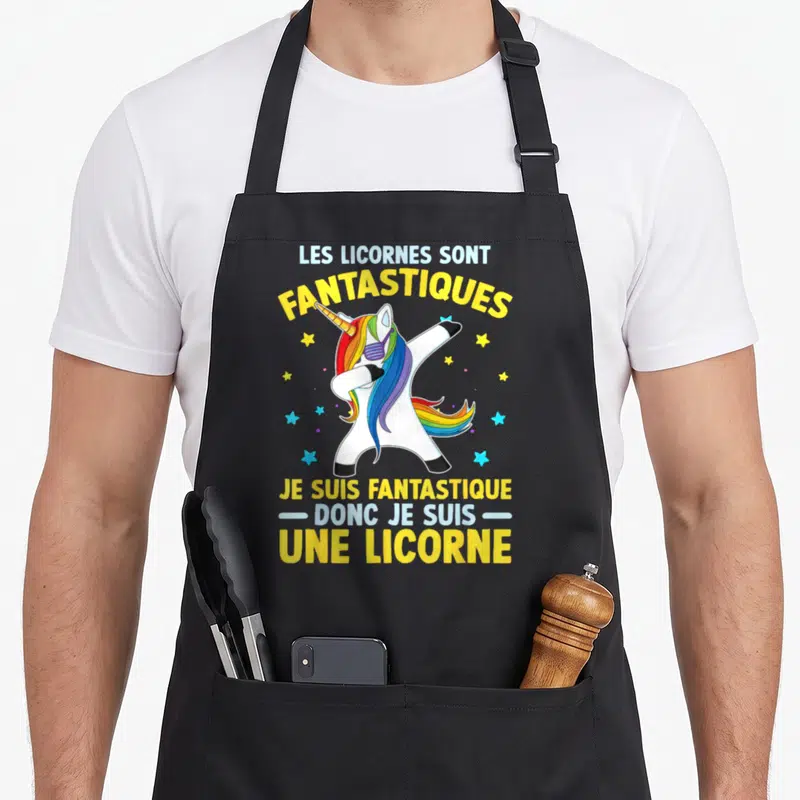 Tablier de cuisine noir avec une licorne colorée effectuant un dab entouré d'étoiles et de textes humoristiques jaunes et bleus.