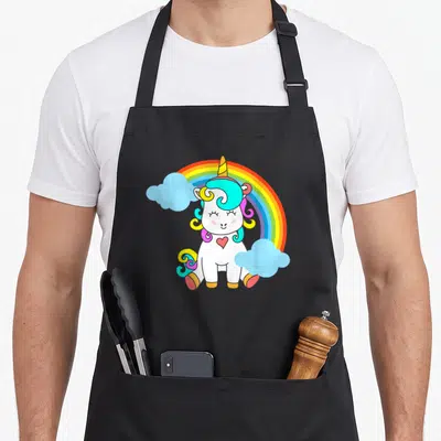 Tablier de cuisine noir avec une licorne blanche souriante, un arc-en-ciel coloré et des nuages bleus en arrière-plan.