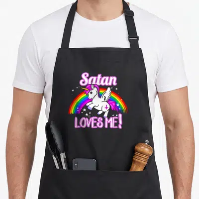 Tablier de cuisine noir avec une licorne ailée blanche, un arc-en-ciel et le texte Satan Loves Me en rose vif.