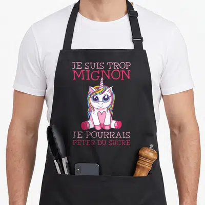 Tablier de cuisine noir avec une licorne rose aux yeux bleus et un texte humoristique en lettres roses.