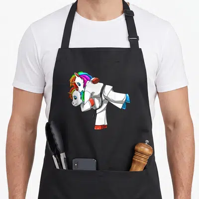 Tablier de cuisine noir avec une licorne en kimono blanc effectuant une prise de judo sur un autre petit poney coloré.