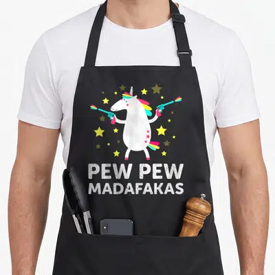 Tablier de cuisine noir avec une licorne tenant des pistolets laser et le texte Pew Pew Madafakas entouré d'étoiles.