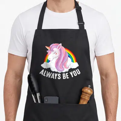 Tablier de cuisine noir avec une licorne rose, un arc-en-ciel et le texte Always Be You en blanc.