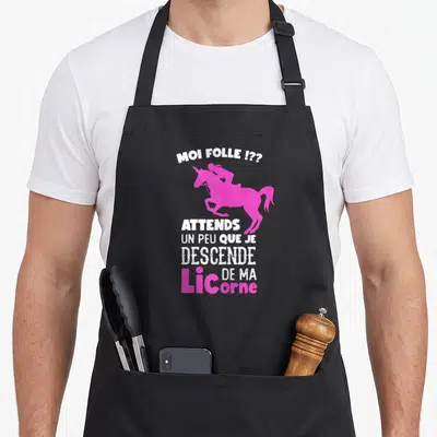 Tablier de cuisine noir avec silhouette licorne rose et texte blanc « Moi folle ? Attends un peu que je descende de ma licorne »