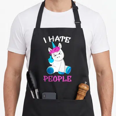Tablier de cuisine noir avec une licorne blanche fâchée levant le majeur et du texte en anglais.