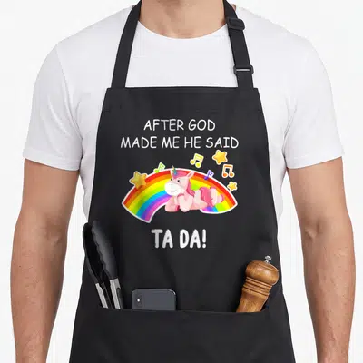 Tablier de cuisine noir avec une licorne rose souriante posée sur un arc-en-ciel et des notes de musique jaunes.