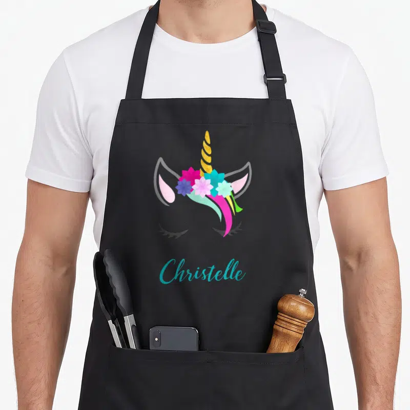 Tablier de cuisine noir avec tête de licorne aux fleurs colorées et le nom Christelle en écriture cursive turquoise.