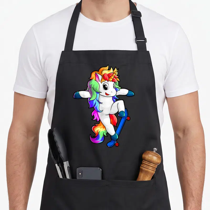 Tablier de cuisine noir avec illustration d'une licorne blanche sur planche à roulettes aux couleurs vives.
