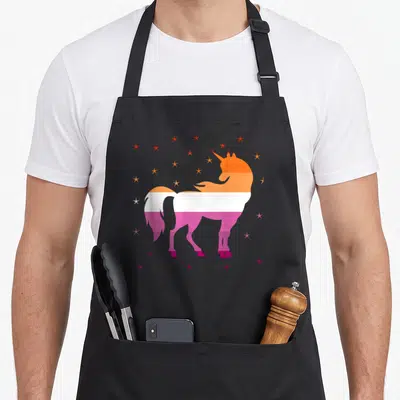 Tablier de cuisine noir avec une licorne aux couleurs du drapeau lesbien et des étoiles multicolores.