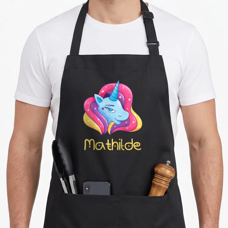 Tablier de cuisine noir avec tête de licorne bleue et prénom Mathilde en lettres jaunes.