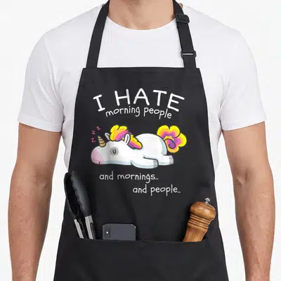 Tablier de cuisine noir avec une licorne blanche aux cheveux colorés et du texte blanc humoristique.