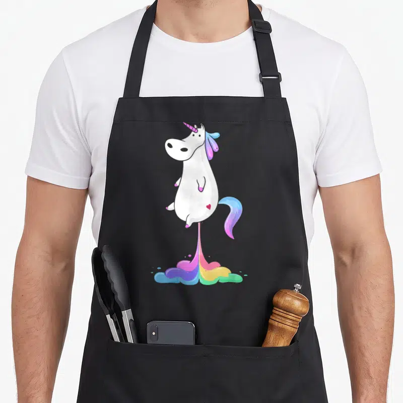 Tablier de cuisine noir avec une illustration de licorne blanche se fondant en arc-en-ciel multicolore.