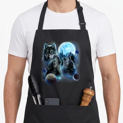 Tablier de cuisine noir avec trois loups hurlants, une grande lune bleue et plusieurs planètes flottantes sur fond sombre.