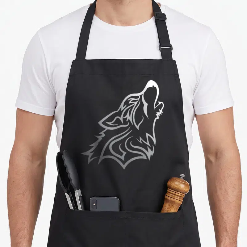 Tablier de cuisine noir avec un motif graphique argenté représentant un loup stylisé en train de hurler vers le ciel.
