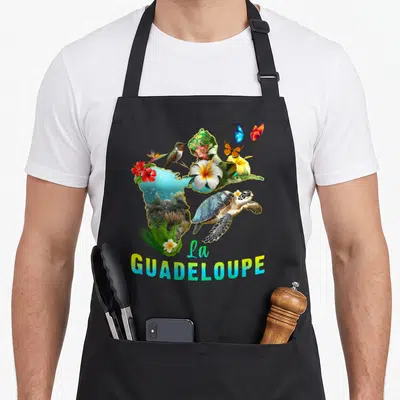 Tablier de cuisine noir avec carte de la Guadeloupe ornée d'une tortue, d'un colibri, de papillons et de fleurs tropicales colorées.