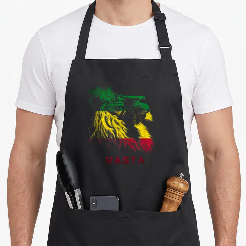 Tablier de cuisine noir avec tête de lion aux couleurs Rastafari et l'inscription RASTA en bas.