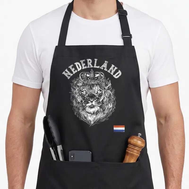 Tablier de cuisine noir avec tête de lion couronné, inscription Nederland et petit drapeau tricolore en bas à droite.