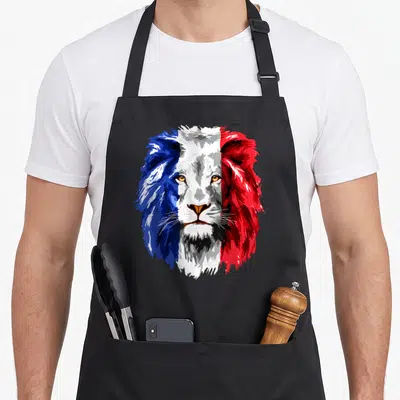 Tablier de cuisine noir avec un visage de lion aux couleurs du drapeau français imprimé en grand sur le devant.