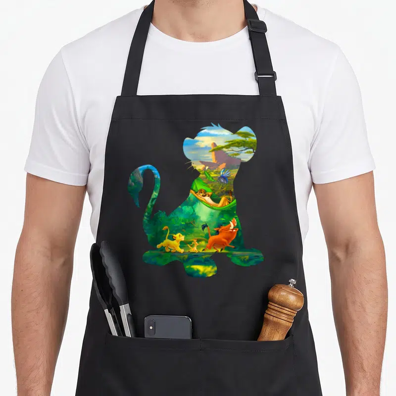 Tablier de cuisine noir avec silhouette de lion remplie de scènes africaines et de personnages animés colorés.