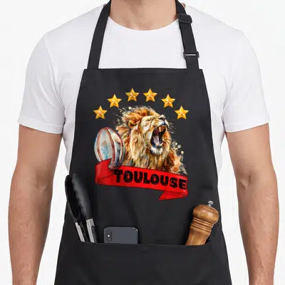 Tablier de cuisine noir avec illustration d'un lion rugissant, six étoiles dorées et le mot Toulouse sur un ruban rouge.