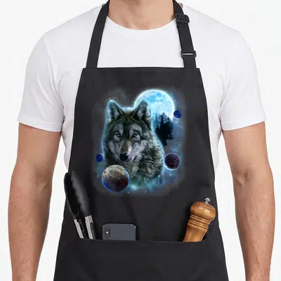 Tablier de cuisine noir avec un loup gris regardant droit devant, des planètes colorées et une grande lune bleue lumineuse dans le dos.