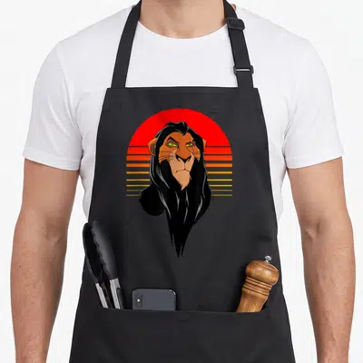 Tablier de cuisine noir avec illustration rétro d'un lion aux yeux verts devant un soleil couchant strié orange et rouge.