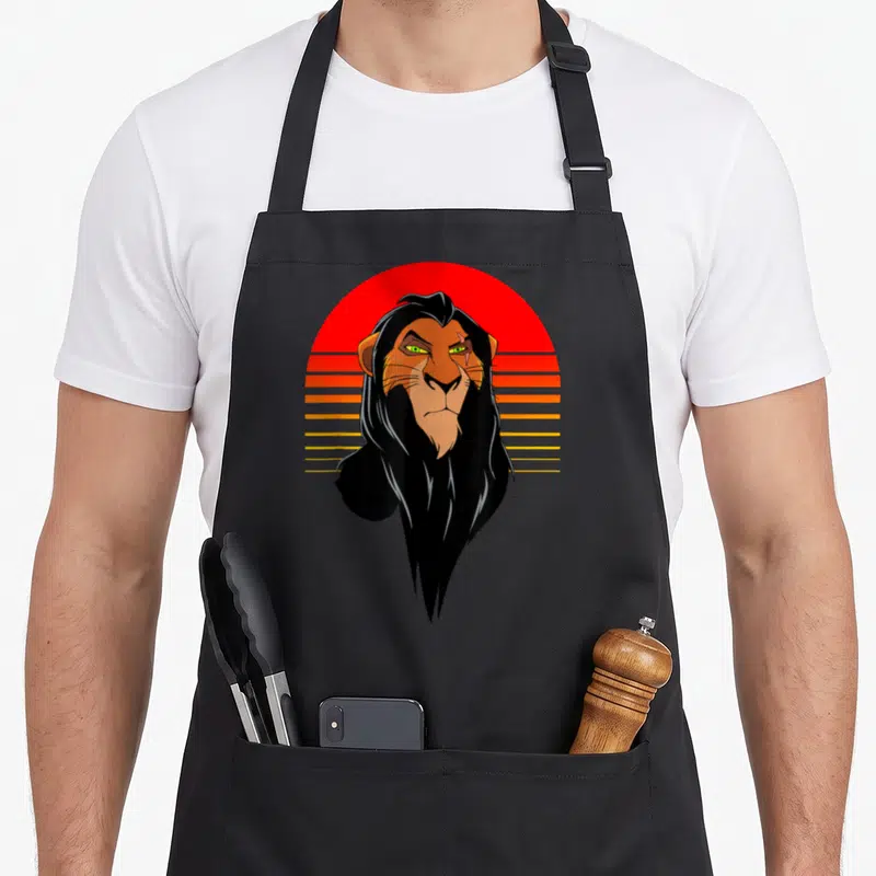 Tablier de cuisine noir avec illustration rétro d'un lion aux yeux verts devant un soleil couchant strié orange et rouge.