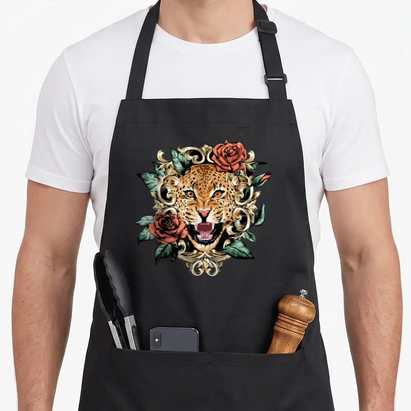 Tablier de cuisine noir avec tête de tigre ornée de roses rouges et motifs baroques dorés.