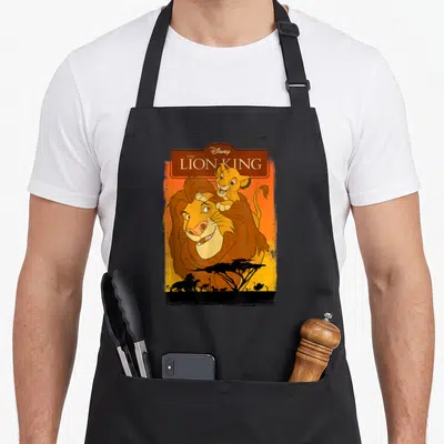 Tablier de cuisine noir avec Simba et Mufasa du Roi Lion sur fond orange et silhouette d'acacia.