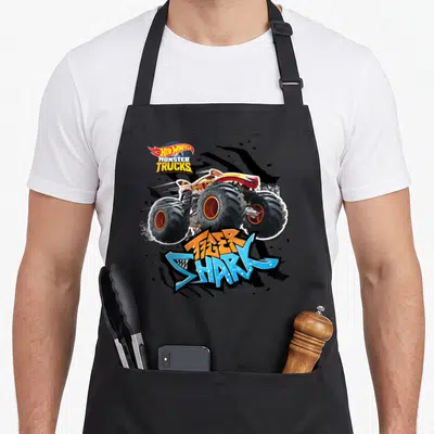 Tablier de cuisine noir avec un monster truck orange Tiger Shark et le logo Hot Wheels Monster Trucks en haut à gauche.