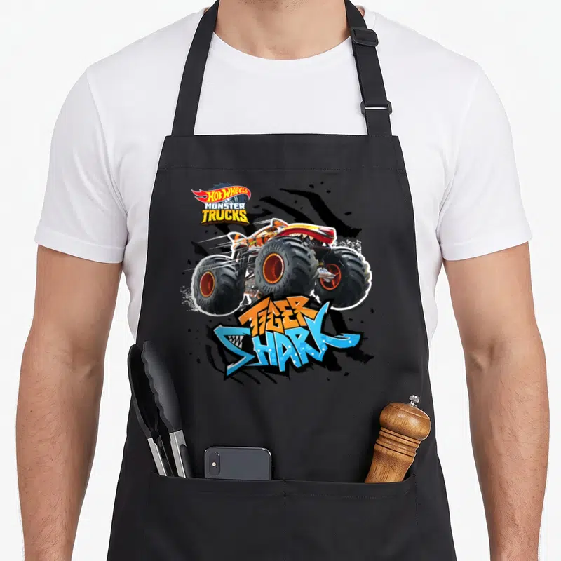 Tablier de cuisine noir avec un monster truck orange Tiger Shark et le logo Hot Wheels Monster Trucks en haut à gauche.