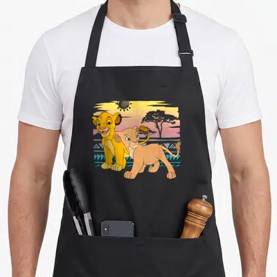 Tablier de cuisine noir avec Young Simba et Nala devant un soleil et un arbre d'acacia au crépuscule.
