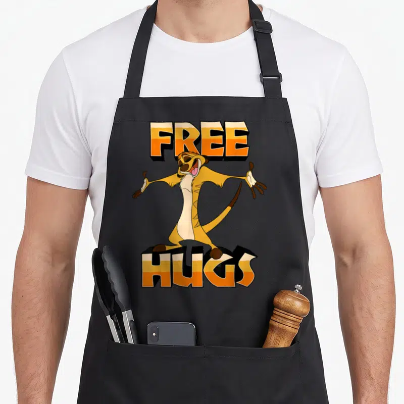 Tablier de cuisine noir avec Timon les bras ouverts et l'inscription FREE HUGS en lettres orange et blanches.
